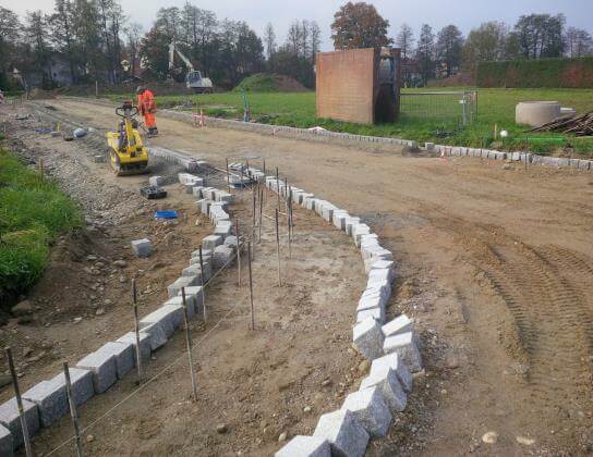 Bauarbeiten am neuen Wohngebiet Fahnbacher Straße Süd in Haiming, Bayern, mit Baustellenfahrzeugen und umgebender Landschaf