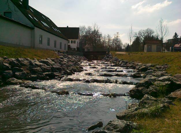 Renaturierte Uferzone mit Pflanzen und einem klaren Gewässer im Projekt 'Gewässerumgestaltung, Langenneufnach'.